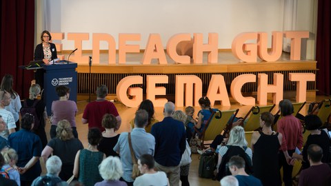 Frau Prof. Böhm spricht neben einer Wand mit dem Schriftzug "Einfach gut gemacht" Davor Zuhörer.