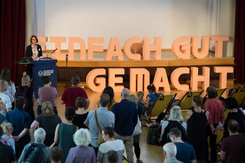 Frau Prof. Böhm spricht neben einer Wand mit dem Schriftzug "Einfach gut gemacht" Davor Zuhörer.