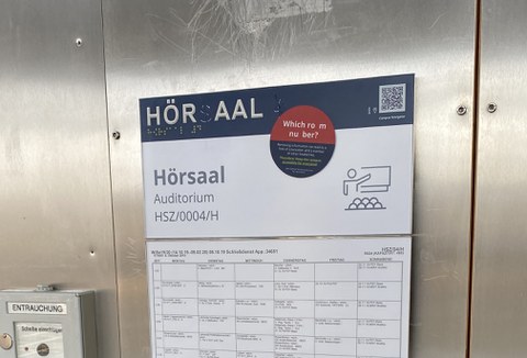 An Profil- und Brailleschrift beschädigtes Türschild vom Hörsaal 4