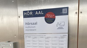 An Profil- und Brailleschrift beschädigtes Türschild vom Hörsaal 4