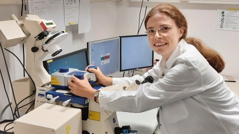 Eine Frau im weißen Kittel arbeitet an einem Mikroskop