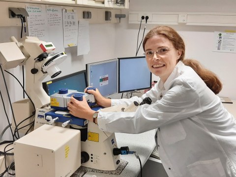 Eine Frau im weißen Kittel arbeitet an einem Mikroskop