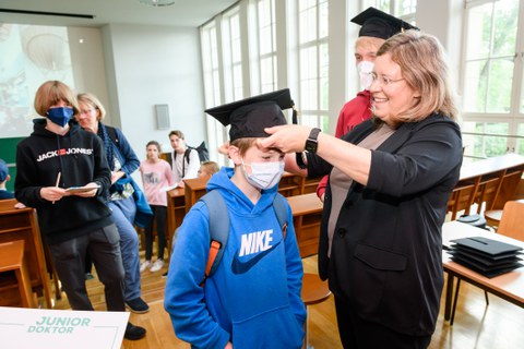 Eine Frau setzt einem Kind einen Doktorhut auf den Kopf.