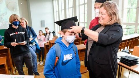 Eine Frau setzt einem Kind einen Doktorhut auf den Kopf.