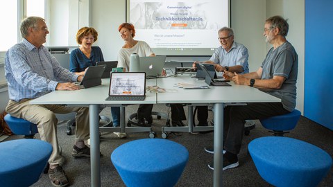 Um einen Tisch sitzen 5 ältere Personen vor Laptops.