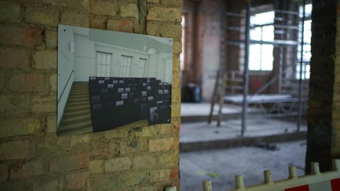 Eine Leichtbauwand vor einem in Bau befindlichen Raum. An der Wand eine Grafik des fertigen Raums.
