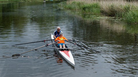 Ruderboot auf einem Fluss, darin eine junge Frau und ein Mann