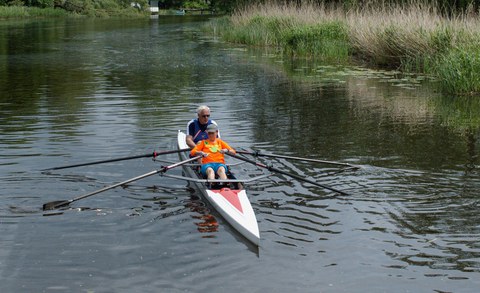 Ruderboot auf einem Fluss, darin eine junge Frau und ein Mann