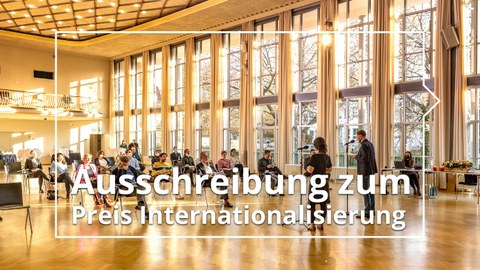 Personen sitzen im Festsaal Dülferstraße, darüber der Schriftzug "Apply now! Internationalization Award""