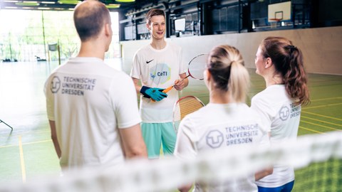vier Badmintonspieler:innen in einer Sporthalle stehen im Kreis. Einer trägt den CeTI-Datenhandschuh