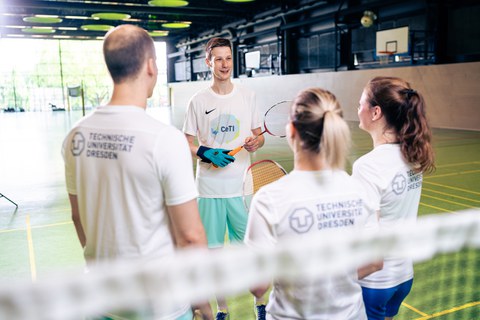 vier Badmintonspieler:innen in einer Sporthalle stehen im Kreis. Einer trägt den CeTI-Datenhandschuh