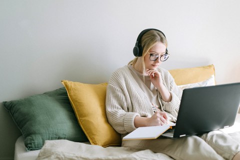 Junge Frau sitzt auf dem Sofa, ein Laptop auf den Knien.