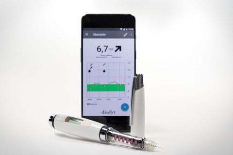 In der Mitte ein gerade stehendes Handy, auf dem Display die geöffnete diafyt-App. Davor liegt eine geöffnete Diabethes-Spritze (Pen).