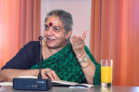 Dr. Vandana Shiva sitzt an einem Tisch und spricht.