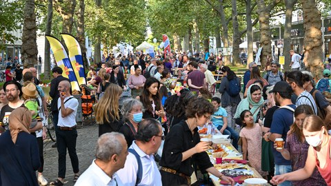 Viele Menschen unterschiedlicher Herkunft sitzen gemeinsam an langen Tischen.