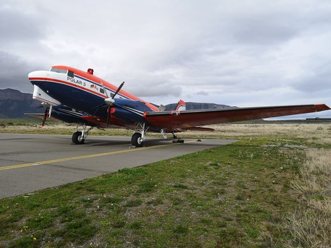 Ein Kleinflugzeug steht auf einer Landebahn, daneben eine Wiese