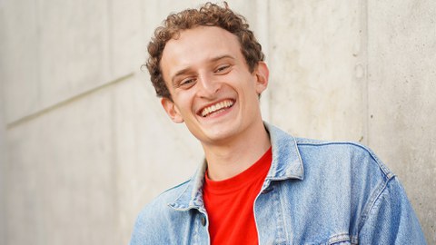 Ein junger Mann mit blonden Locken lächelt in die Kamera,