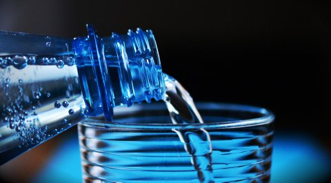 Aus einer Glasflasche wird Wasser in ein Glas gefüllt.