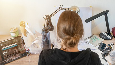 Blick über den Rücken einer Frau auf einen Schreibtisch.