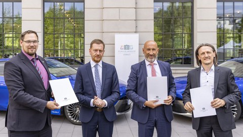 Vier Herren im Anzug mit einer Urkunde in der Hand.