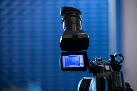 Eine Kamera steht vor einerblauen Wand mit TUD-Logos.