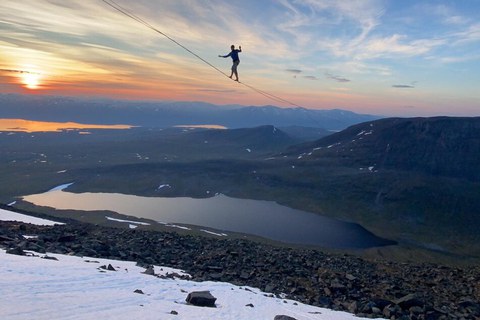 Bergige Landschaft, darüber ein Mensch auf einer Slackline.