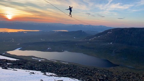 Bergige Landschaft, darüber ein Mensch auf einer Slackline.