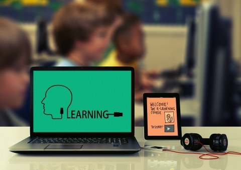 Links in aufgeklappter Laptop, darauf auf grünem Untergrund das Wort "Learning". Rechts daneben ein Tablett, ein Smartphone am Kabel und Kopfhörer.