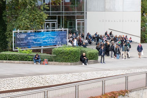 Junge Menschen vor dem Hörsaalzentrum, daneben ein "Willkommen-Banner"