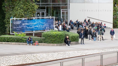 Junge Menschen vor dem Hörsaalzentrum, daneben ein "Willkommen-Banner"