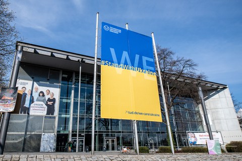 Vor dem Hörsaalzentrum steht ein Banner (oben blau, unten gelb) mit der Aufschrift: We stand with Ukraine