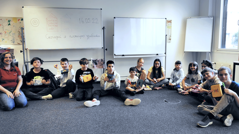 Schüler sitzen mit ihrer Lehrerin im Kreis auf dem Fußboden eines Klassenzimmers.