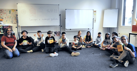 Schüler sitzen mit ihrer Lehrerin im Kreis auf dem Fußboden eines Klassenzimmers.