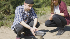 Zwei Personen identifizieren mithilfe eines Siebes Ameisenlöwen im Sand.