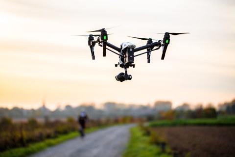 Eine Drohne fliegt über eine Straße, im Hintergrund eine Stadt.