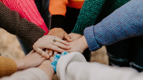 Menschen stehen im Kreis und legen ihre Hände aufeinander (zu sehen sind nur Arme und Hände)