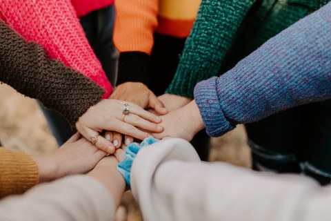 Menschen stehen im Kreis und legen ihre Hände aufeinander (zu sehen sind nur Arme und Hände)