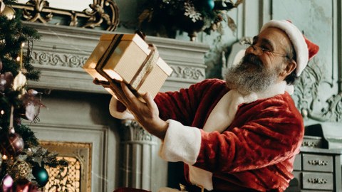 Ein Weihnachtsmann steht vor einem Kamin und hält ein Geschenk in den Händen.