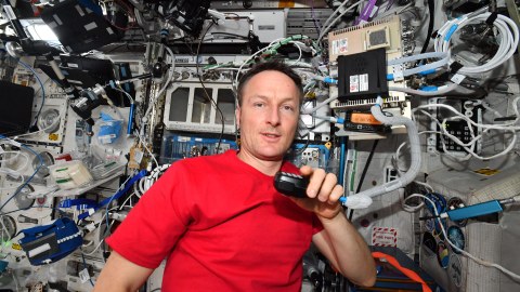 Ein Mann in rotem T-Shirt und einem Funkgerät in der Hand vor einer Wand voll technischer Apparaturen.