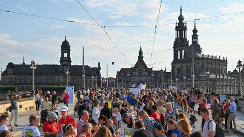viele Menschen sitzen und stehen an langen Tischen Im Hintergrund die Hofkirche.