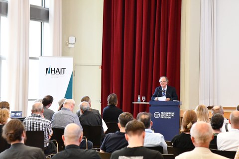 Ein Mann steht am Podium in einem Saal vor vielen Menschen.