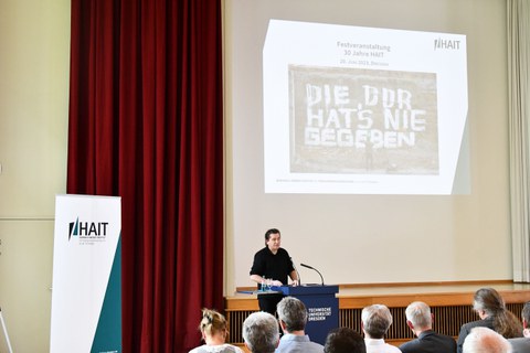 Ein Mann steht am Podium in einem Saal vor vielen Menschen.