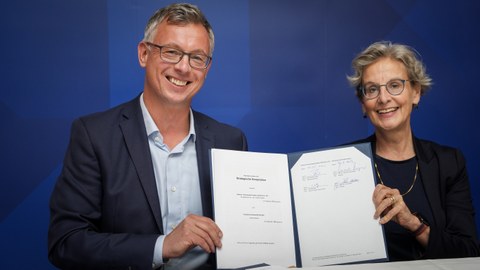 Raik Brettschneider (links) und Prof. Staudinger halten einen unterschriebenen Vertrag in die Kamera.