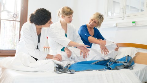 Drei Frauen trainieren an einem Dummy die Umlagerung eines Patienten im Bett.