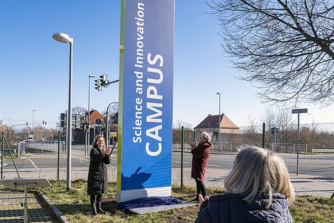 Drei Frauen applaudieren vor einer enthüllten blauen Stele.