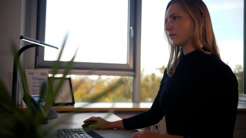 Fotoaufnahme einer Frau, die am Schreibtisch sitzt und mit ihrer rechten Hand eine Computermaus bedient.