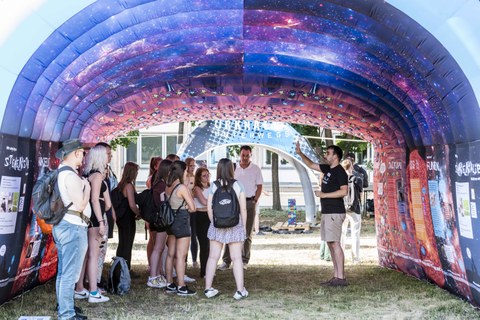 Eine Gruppe von Menschen steht in einem Pavillon, an dessen Decke das Weltall abgebildet ist.