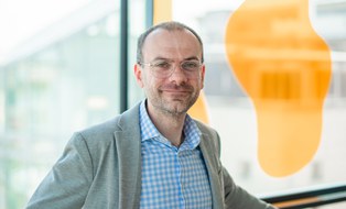 Portrai eines Manns mit hellem Jackett vor einer Fensterscheibe
