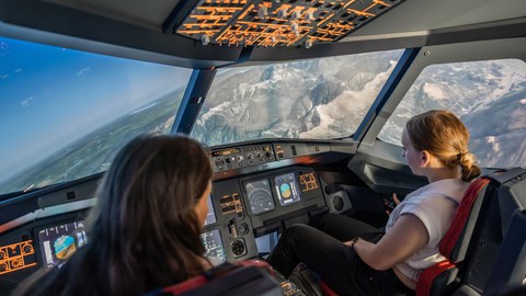 Two young women sit in a flight simulator.