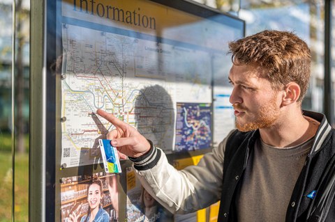 Junger Mann mit einer Campuscard in der Hand steht vor einem Verkehrsplan der Dresdner Verkehrsbetriebe.